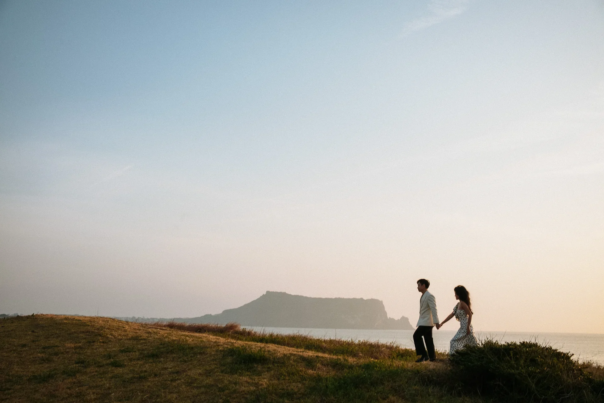 Vũ and Thi silhouetted on a sunset clifftop overlooking the ocean
