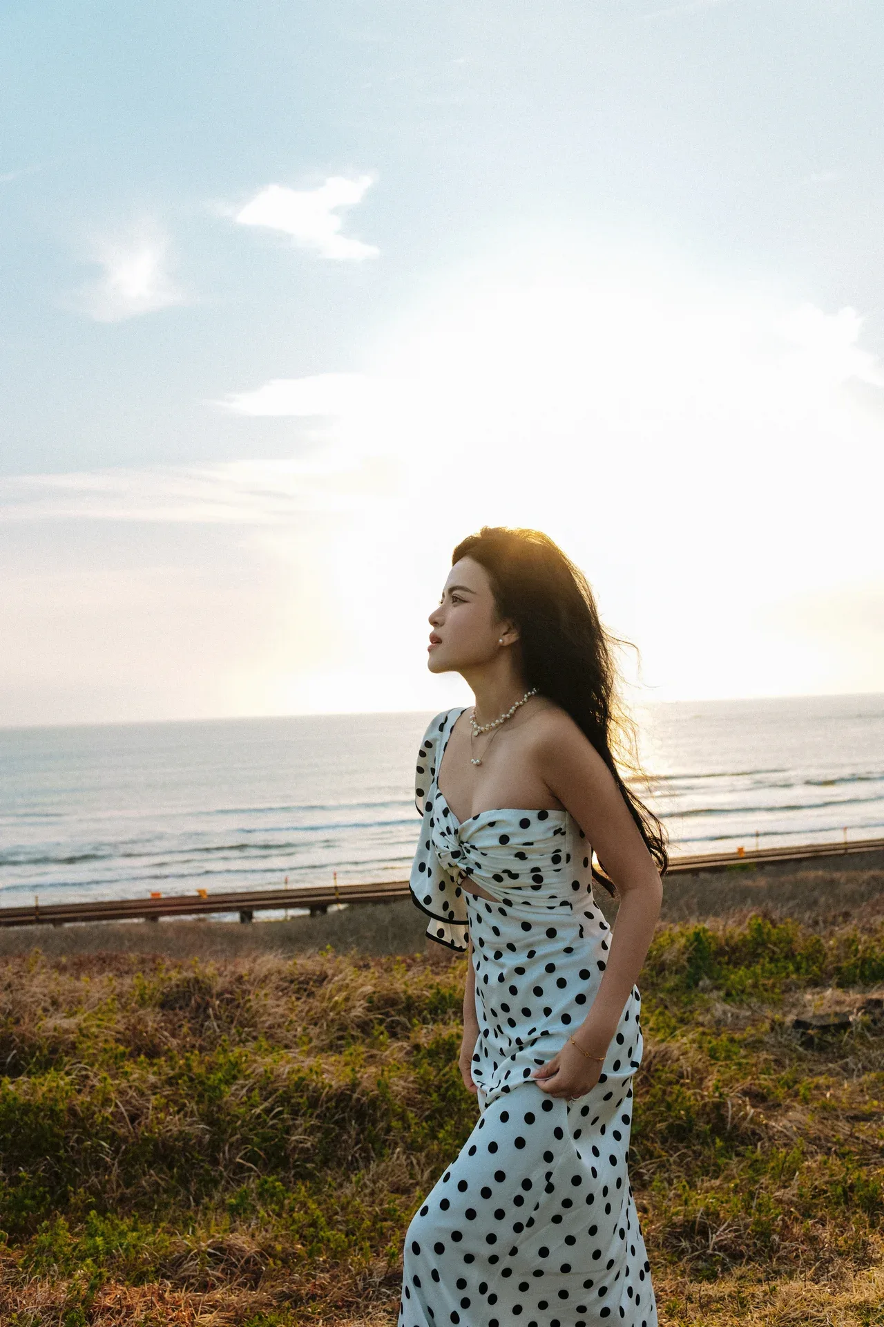 Thi in polka dot dress gazing at the sunset coast